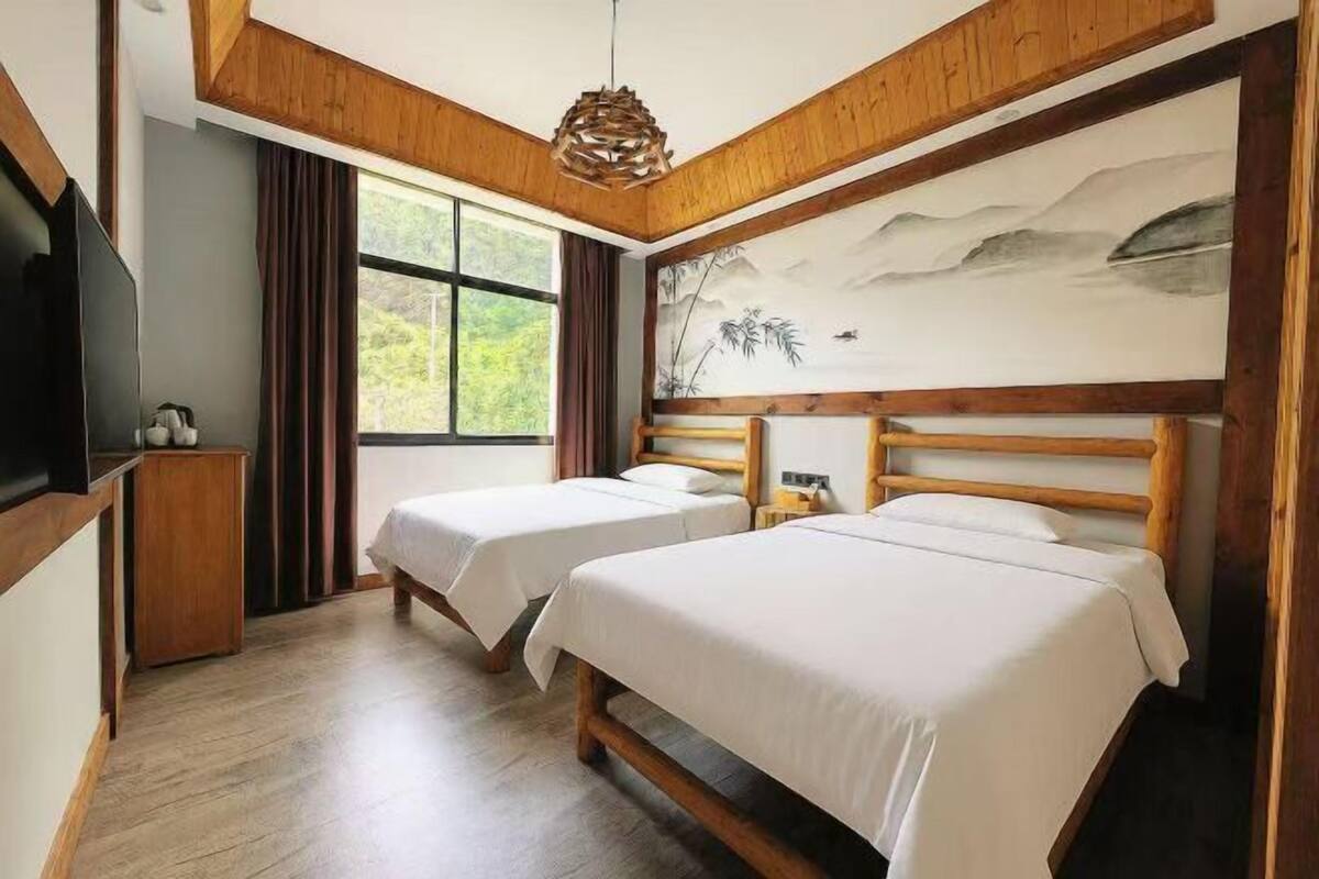 A room with two beds, a TV, a painting, and a window.