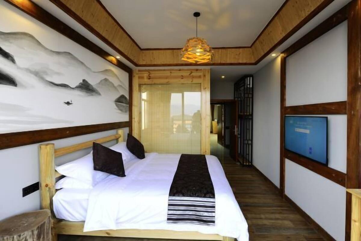 A bedroom with a bed, a wooden headboard, a wall mural, a television, and a wooden floor.