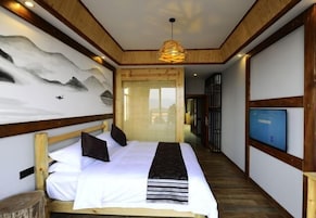 Un dormitorio con cama, cabecera de madera, un mural en la pared, televisor y piso de madera.