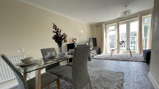 A dining area with a glass table, grey upholstered chairs, and a grey shaggy rug. - Enjoy Lovely 4 bed Apartment With Garden (London)