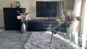 A modern living room with a flat-screen TV, a black entertainment unit, and two vases with flowers. - Enjoy Lovely 4 bed Apartment With Garden (London)