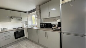 A modern kitchen with stainless steel appliances, white cabinetry, and a window providing natural light. - Enjoy Lovely 4 bed Apartment With Garden (London)