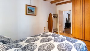 Een slaapkamer met een bed, een houten kledingkast, een deur naar een andere kamer en een lijst met een afbeelding aan de muur.