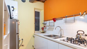 Een kleine keuken met witte kastjes, een roestvrijstalen spoelbak, een waterkoker en een rode waterkoker op het fornuis.