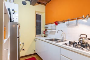 Une cuisine compacte avec des meubles blancs, un évier en acier inoxydable, une bouilloire et une autre bouilloire rouge posée sur la cuisinière.