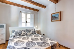 A bedroom with a bed, a window, a bedside table, and a framed picture on the wall.
