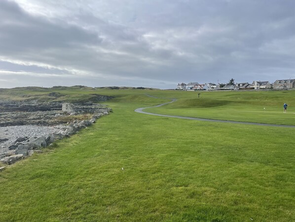 A golf course with a stone wall and houses in the background. - Beautiful 3-bed House in Sunny Killough Down (Downpatrick)