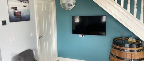 A room with teal walls, a white door, a clock, a flat-screen TV, a wooden barrel, and a gray chair.