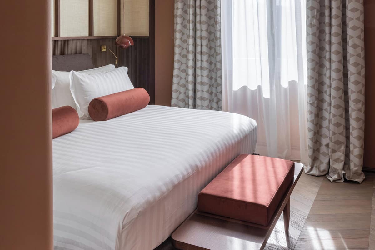 A neatly made bed with white bedding and two pink pillows, a bedside table, and a headboard.