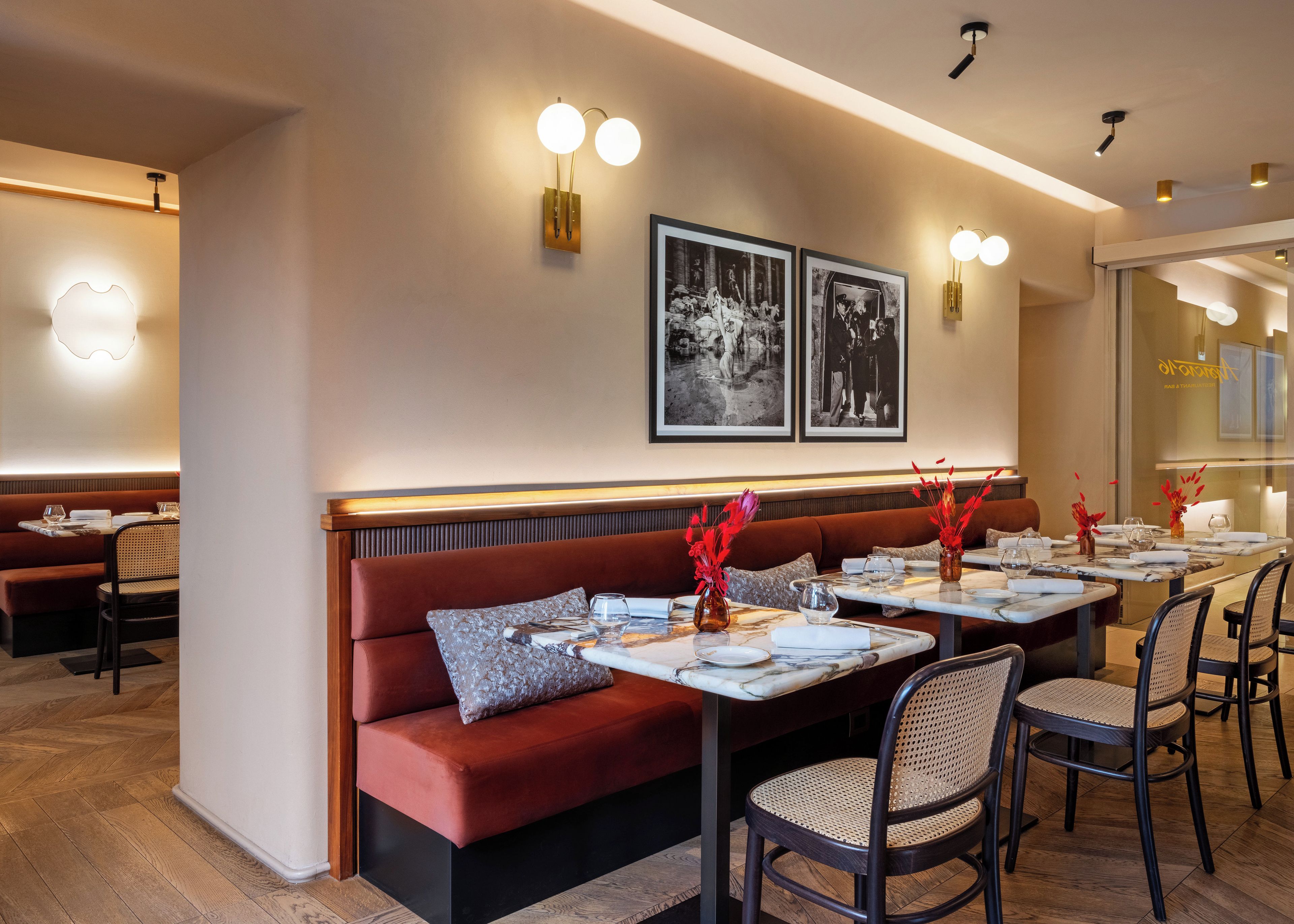 L'intérieur d'un restaurant, avec des banquettes, des tables et des luminaires fixés aux murs.
