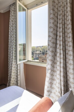 A hotel room with a bed, a window with patterned curtains, and a view of buildings outside. - Palazzo Velabro, a Member of Design Hotels (Rome)