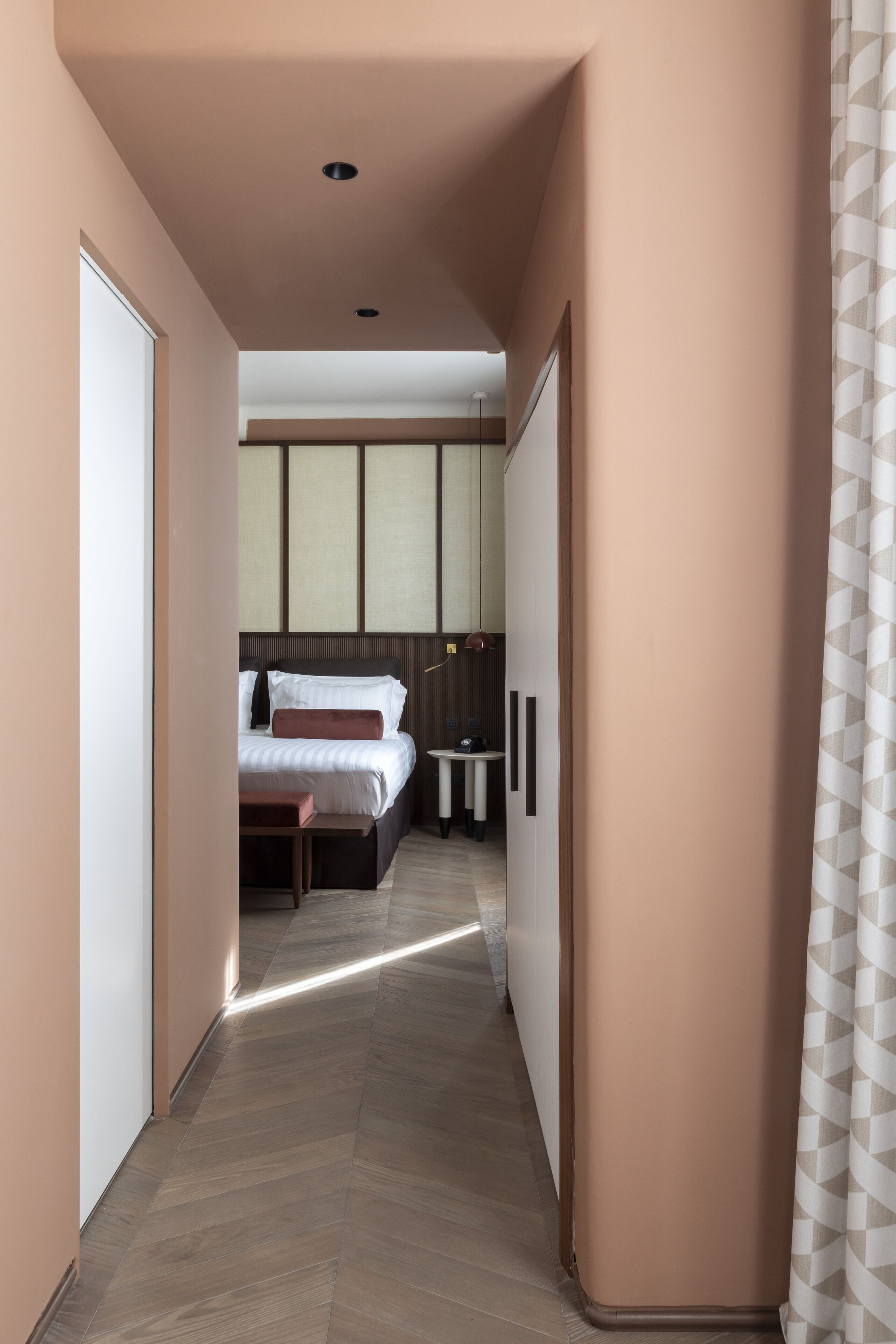 A hallway leading to a bedroom with a bed, bedside tables, and a wardrobe.