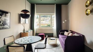 Una sala de estar moderna con una mesa redonda de comedor, un sofá morado y vistas de la ciudad a través de un ventanal.