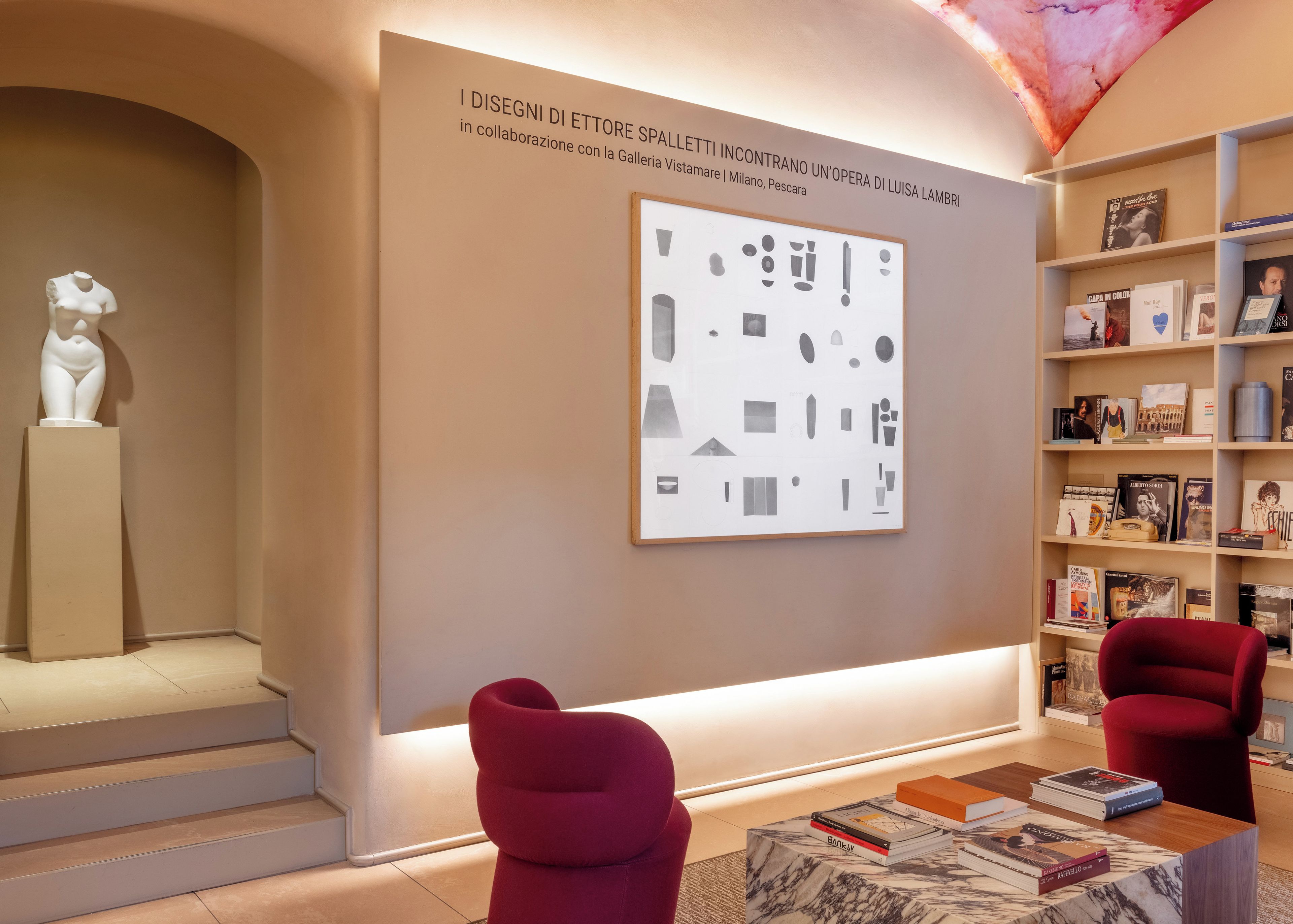 Un interno moderno con un design minimalista, che include una scultura, un'opera d'arte astratta incorniciata e una libreria con libri e oggetti decorativi.