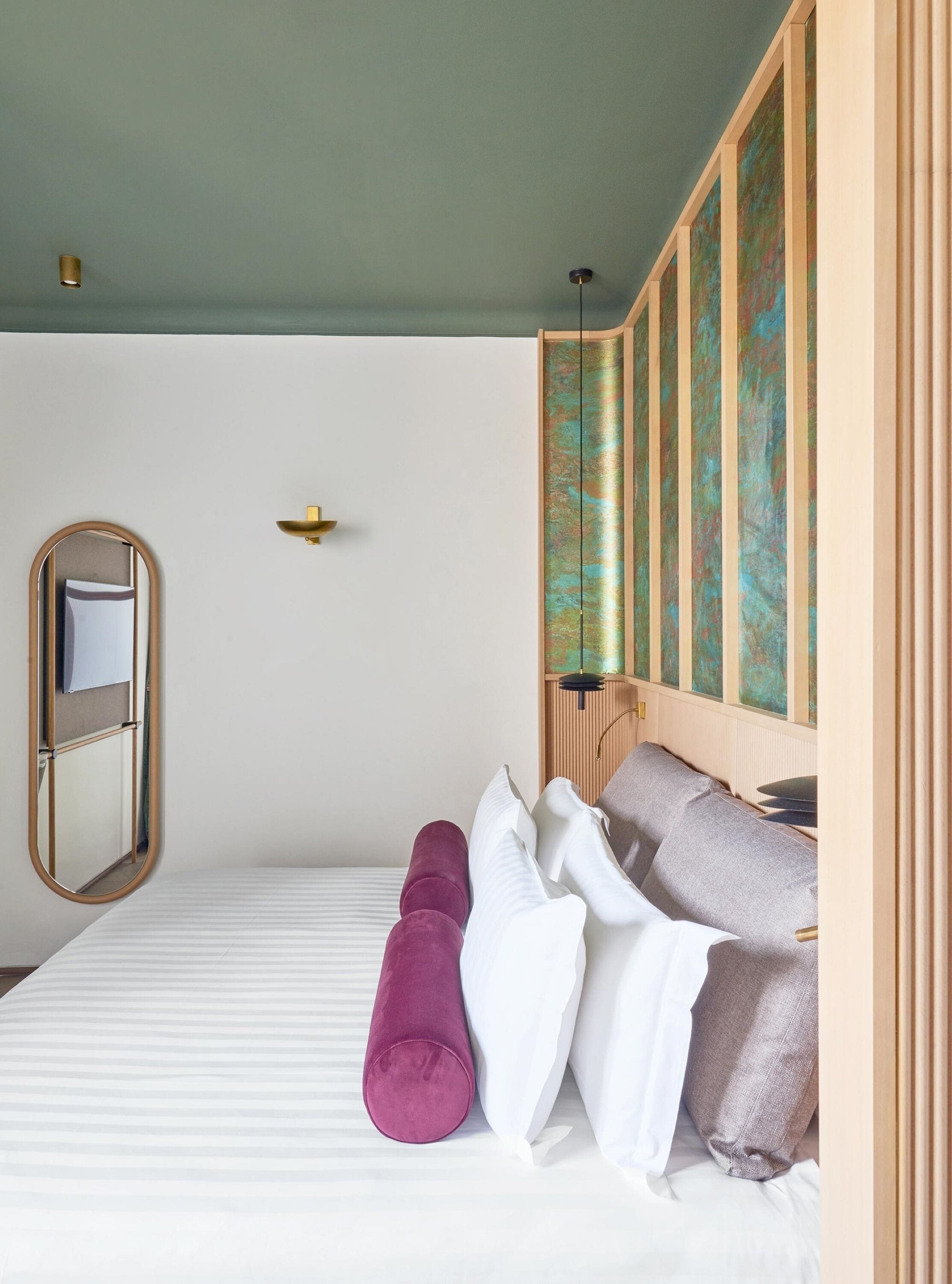 A neatly arranged hotel room with a bed, pillows, a mirror, and a wall-mounted artwork.