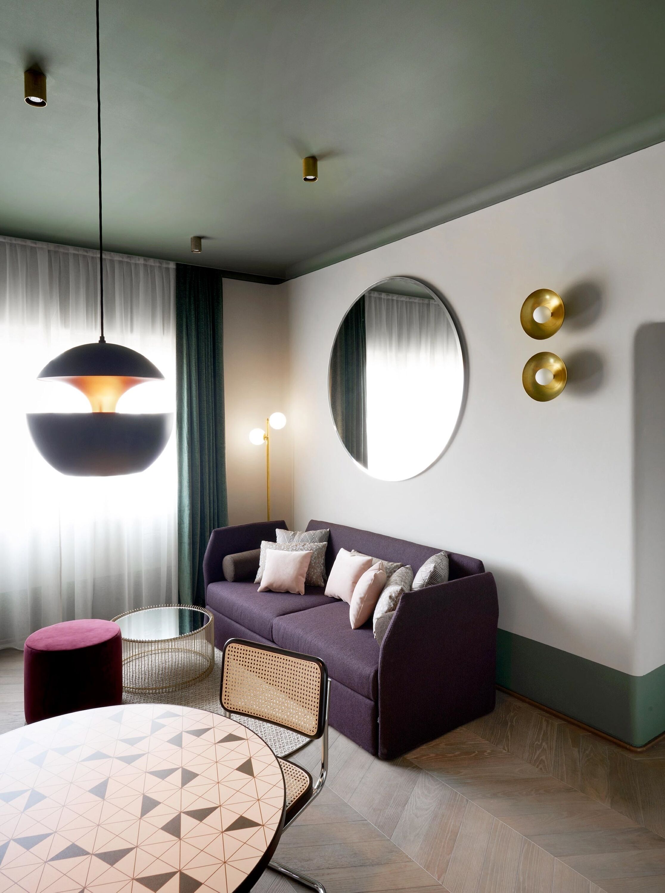 A modern living room with a purple sofa, round mirror, and a table with geometric-patterned chairs.