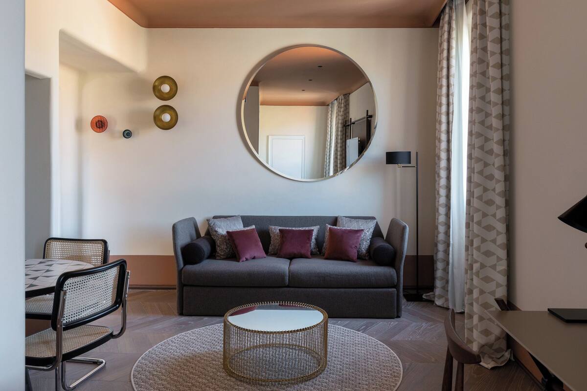 A modern living room with a grey sofa, round coffee table, and a large mirror on the wall.