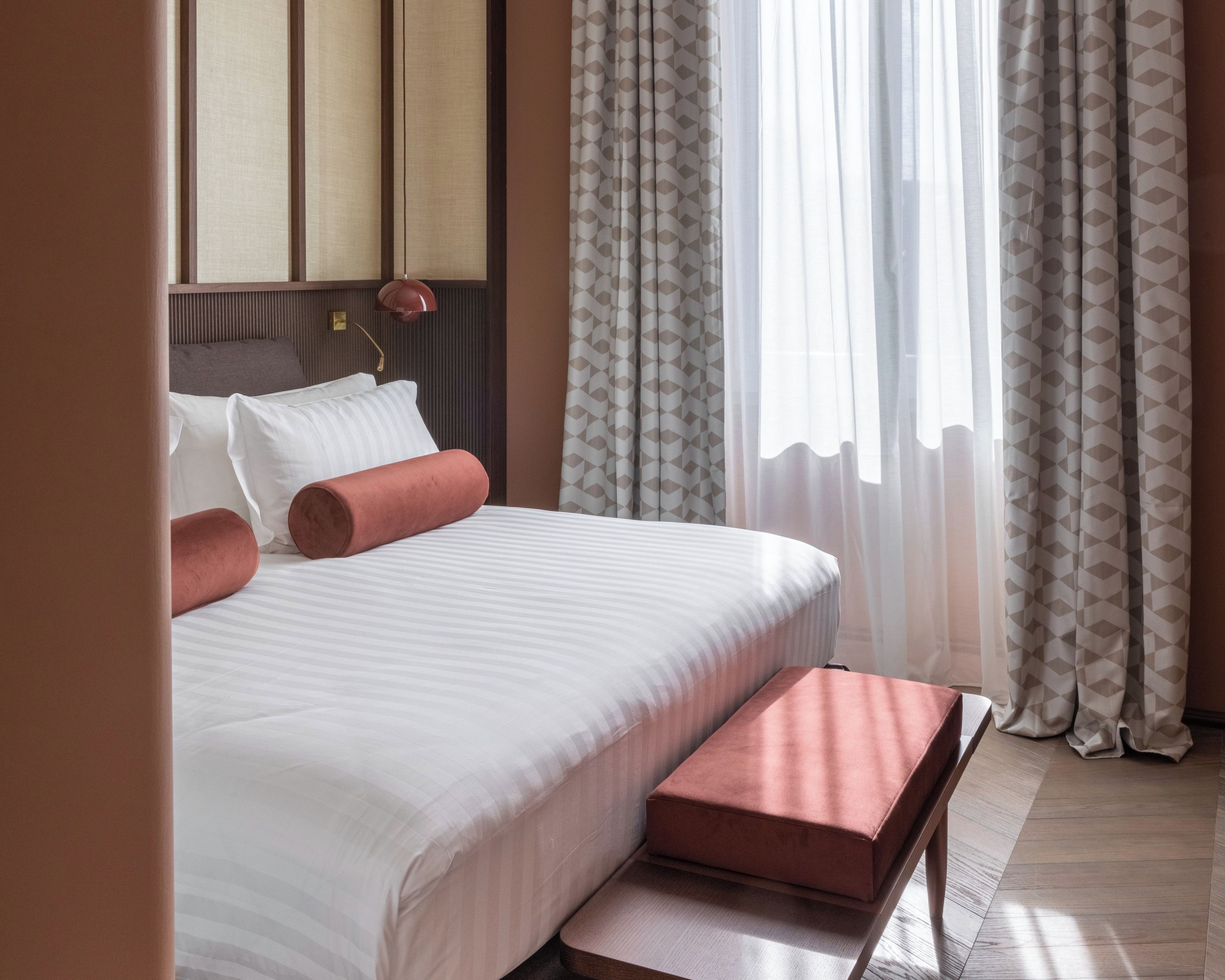 A hotel room with a bed, pillows, a bedside table, and curtains.