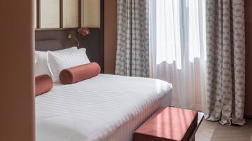 A hotel room with a bed, pillows, a bedside table, and curtains.