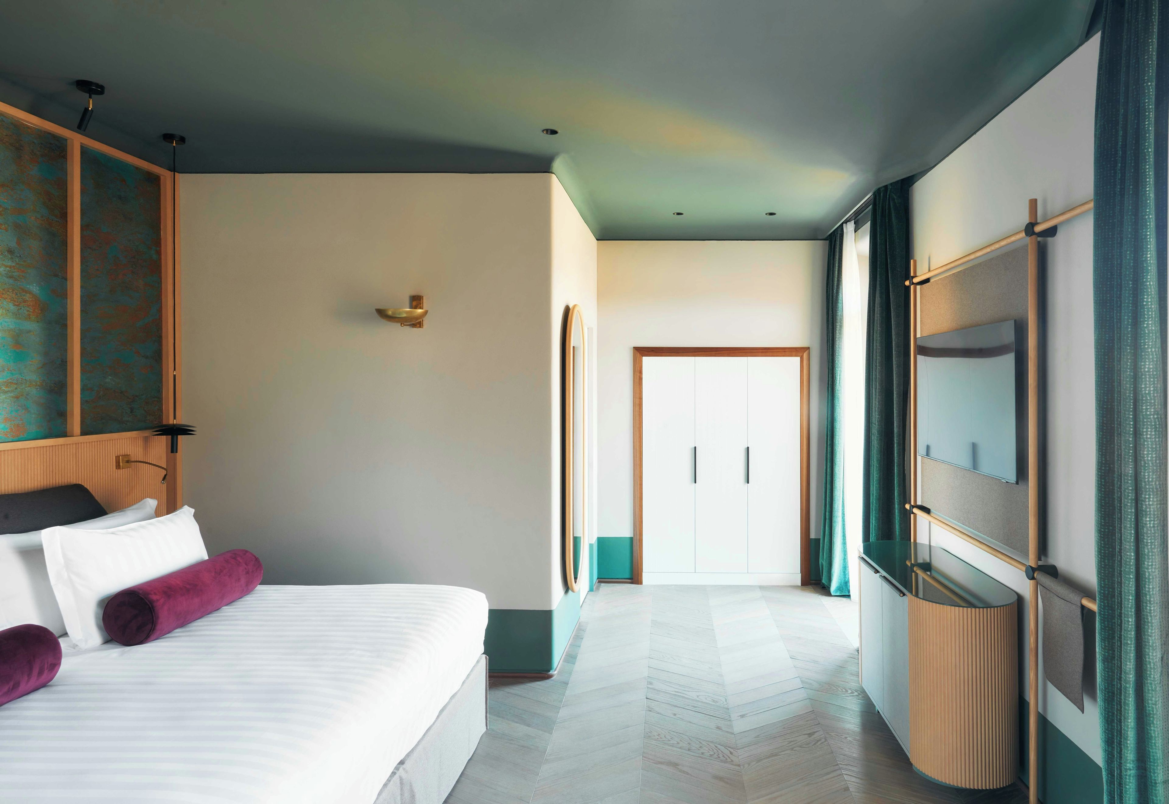 Une chambre d’hôtel avec un lit, un miroir, un téléviseur fixé au mur et une porte donnant sur une autre pièce.