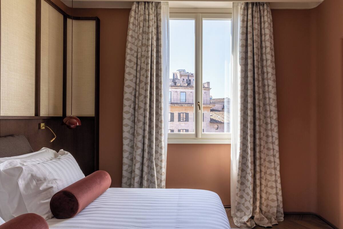 A hotel room with a bed, a nightstand, a mirror, and a window with curtains.