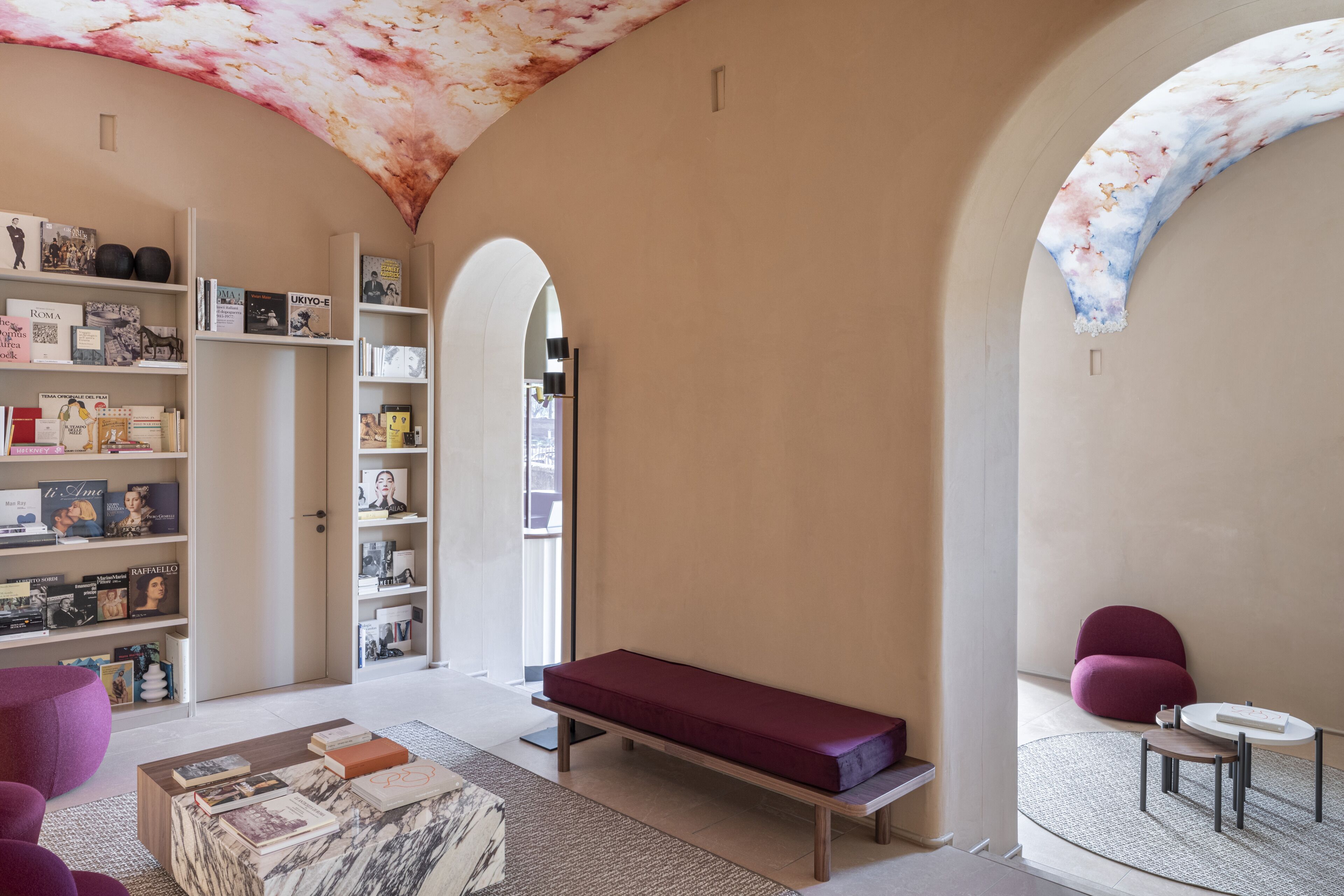 Un interior moderno con una mesa de centro de mármol, un banco rojo y estanterías llenas de libros.