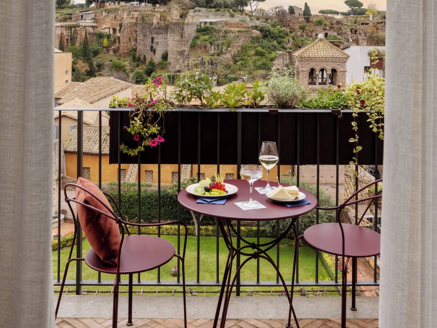 Een balkon met een tafel gedekt voor twee, met uitzicht op een historisch stadsbeeld met oude ruïnes en moderne gebouwen.