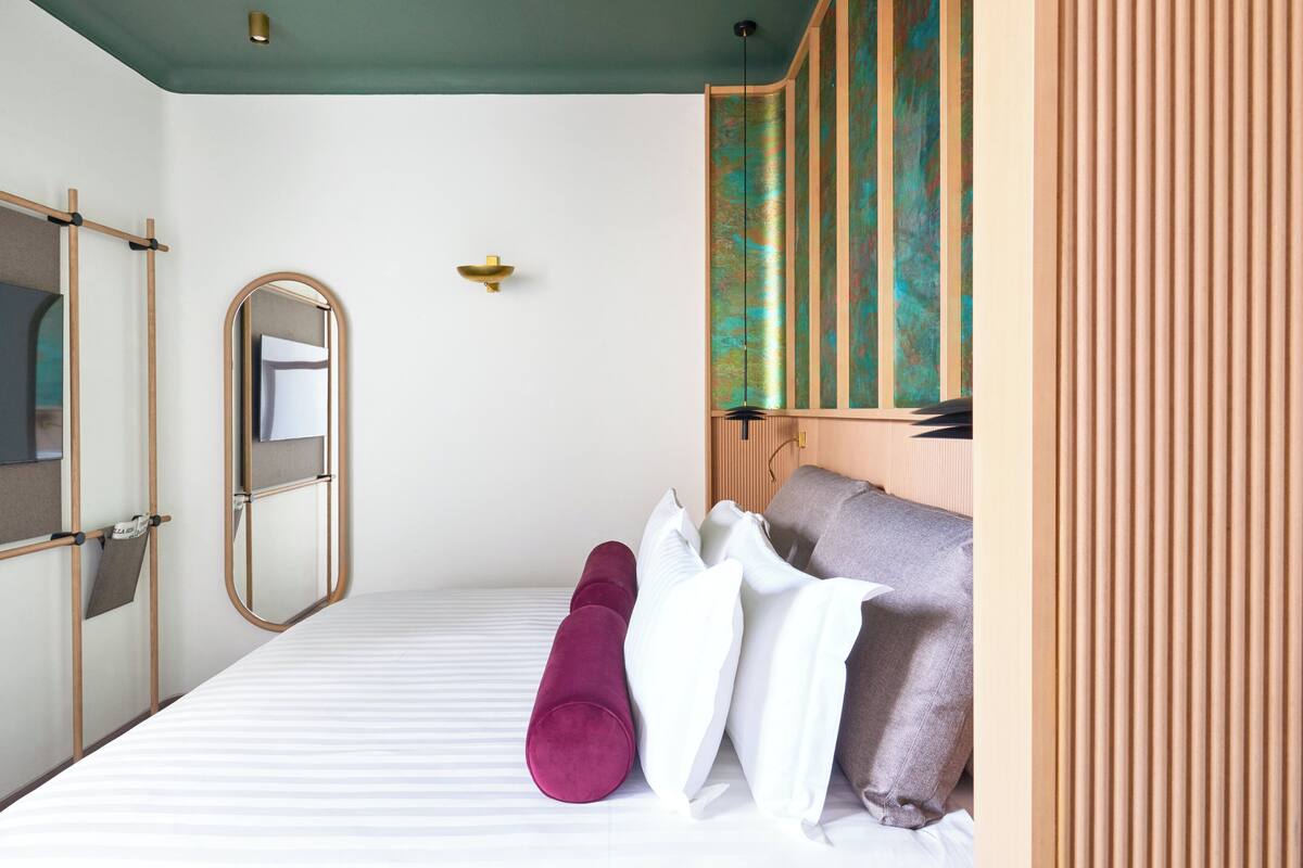 A hotel room with a bed, pillows, a mirror, and a wooden headboard.