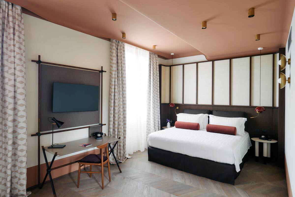 A modern hotel room with a large bed, a desk, and a TV.