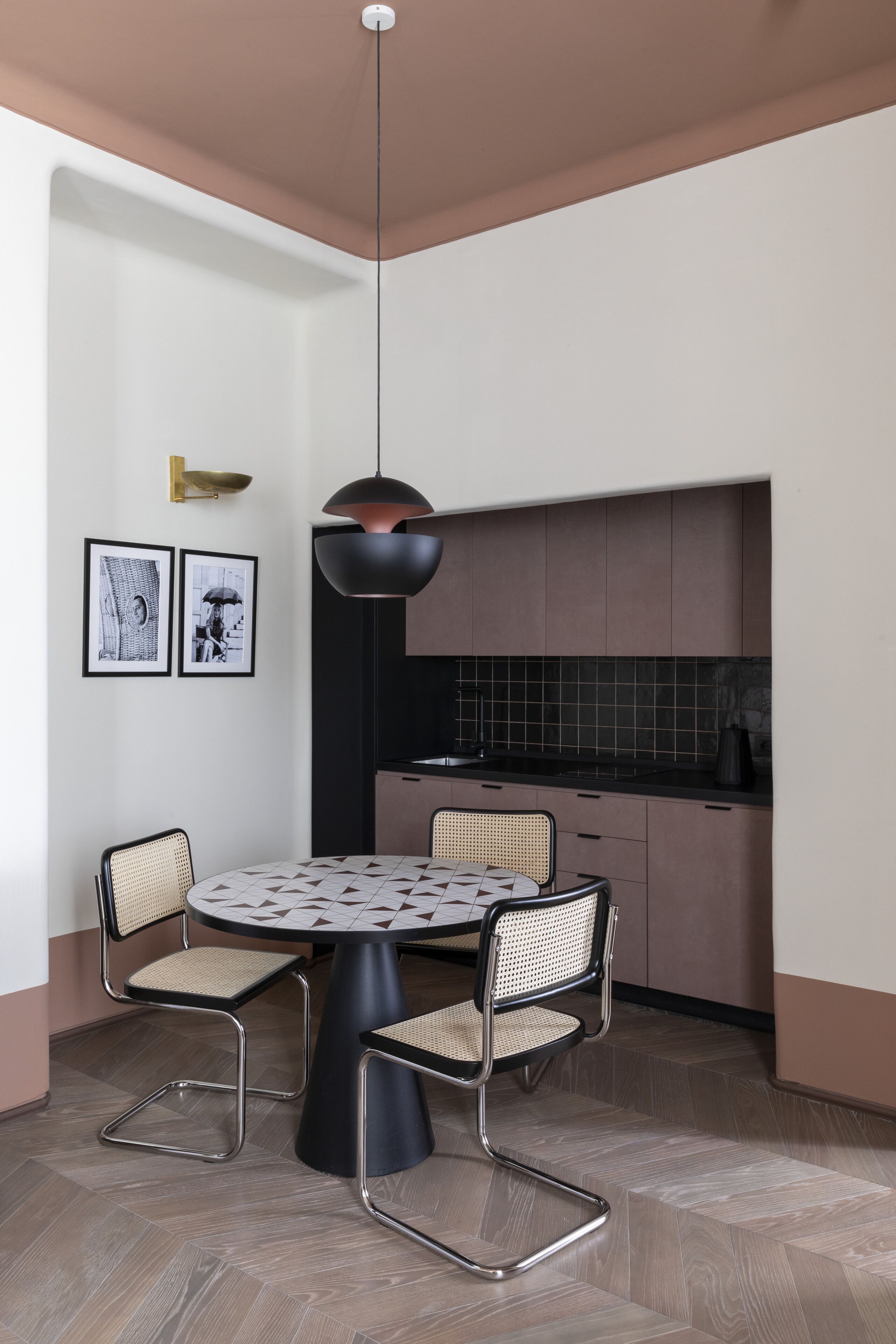 Cozinha moderna com mesa de jantar redonda e quatro cadeiras, luminária pendente e painel de proteção.