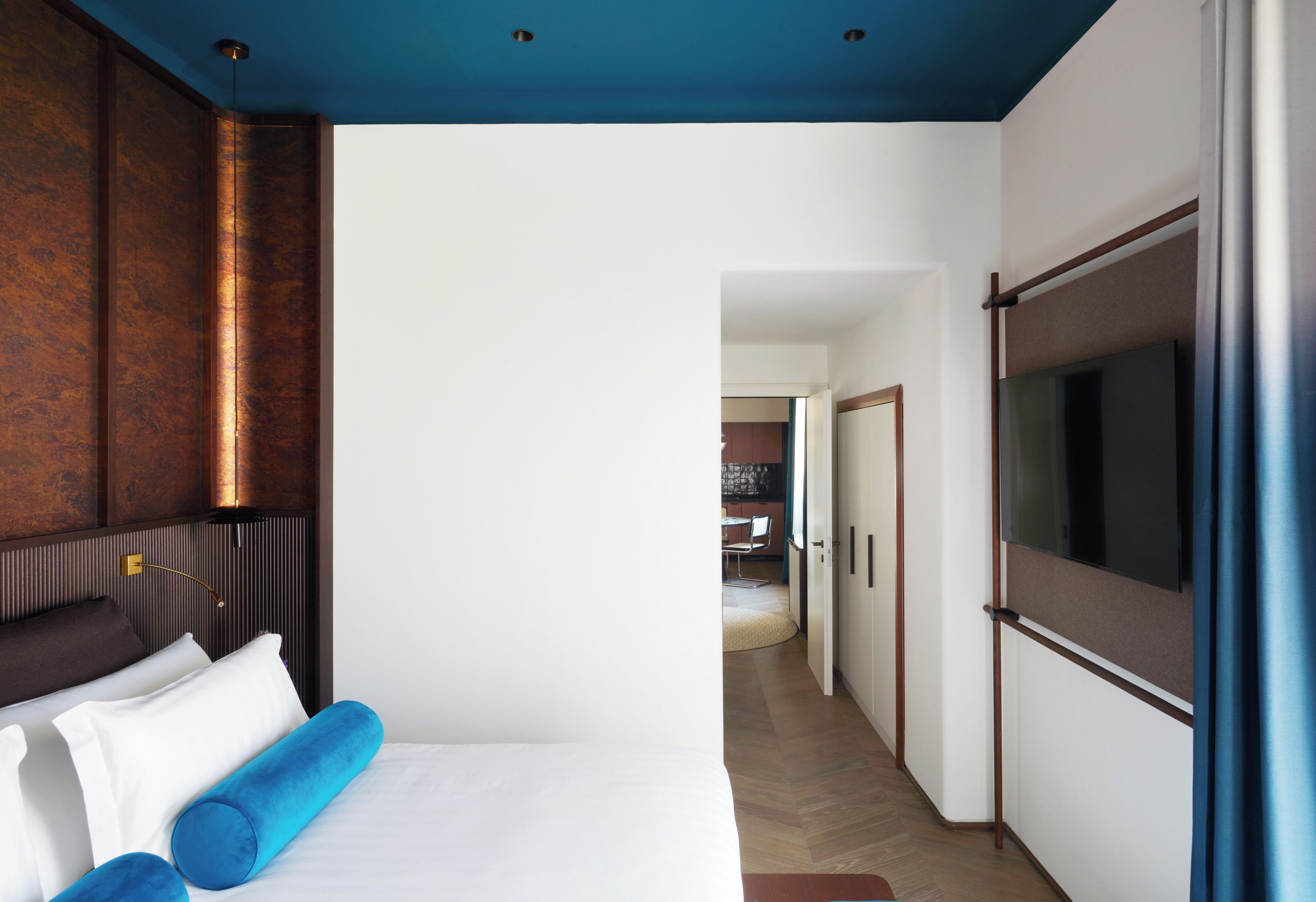 A hotel room with a bed, a television, and a view into the adjacent room.