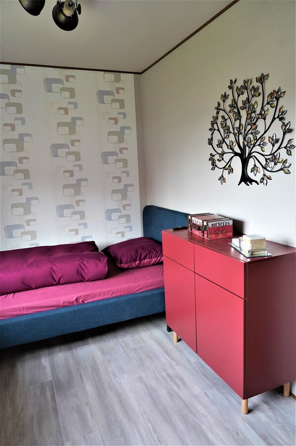 A room with a blue sofa, a red cabinet, and a wall with a tree decal. - Gasthaus Paula (Üdersdorf)