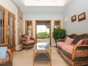 Una stanza con mobili in vimini, un tavolo con piano in vetro e vista su uno spazio all'aperto attraverso una porta.