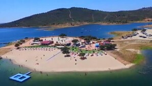 An aerial view of a coastal resort with a sandy beach, several buildings, and boats in the water.