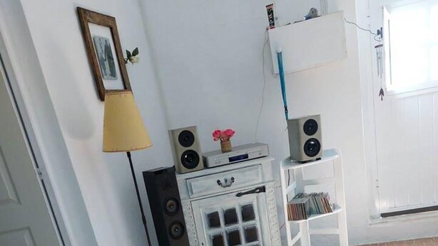 A room with a tiled floor, a white cabinet with drawers, a small table with speakers, and a lamp.
