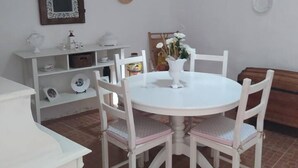 A dining area with a white round table and chairs, a white cabinet with shelves, and a wooden bench.