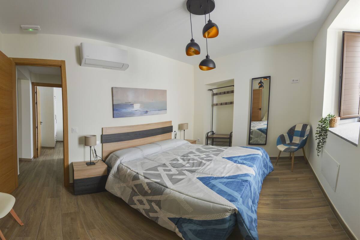 Une chambre à coucher avec un lit, des tables de chevet, une chaise, un miroir et une fenêtre.