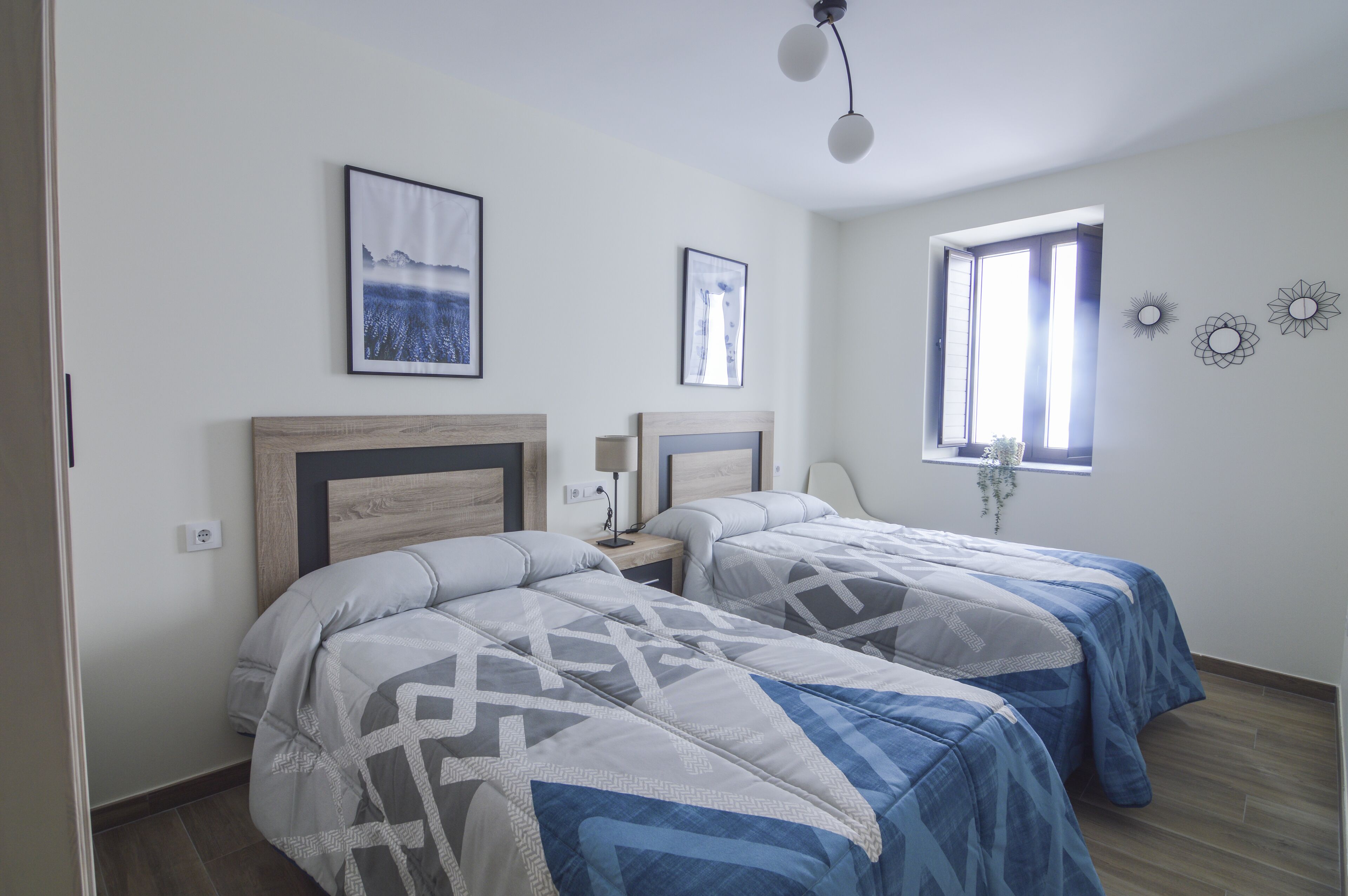 A bedroom with two beds, a nightstand, a lamp, and a window with a view.