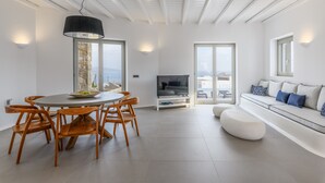 Ein modernes Wohnzimmer mit Essbereich, Fernseher und einer Couch mit Kissen.
