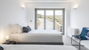 Ein modernes Schlafzimmer mit einem großen Bett, einem Sessel und Blick auf einen steinbelagten Weg.