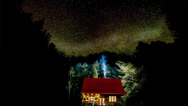 Una cabana amb teulada vermella, envoltada d'arbres, sota un cel estrellat.