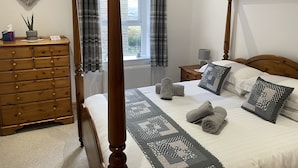 Una cama con dosel con colcha, un aparador de madera y una decoración con forma de corazón en la pared.