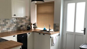 Una cocina con armarios blancos, encimera de madera, lavavajillas, fregadero y una ventana con persianas.