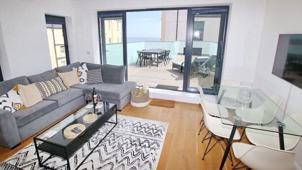 A modern living room with a grey sofa, a glass coffee table, and a dining area with a glass table and chairs.