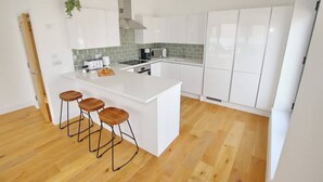 A modern kitchen with white cabinetry, a central island with stools, a green-tiled backsplash, and wooden flooring.