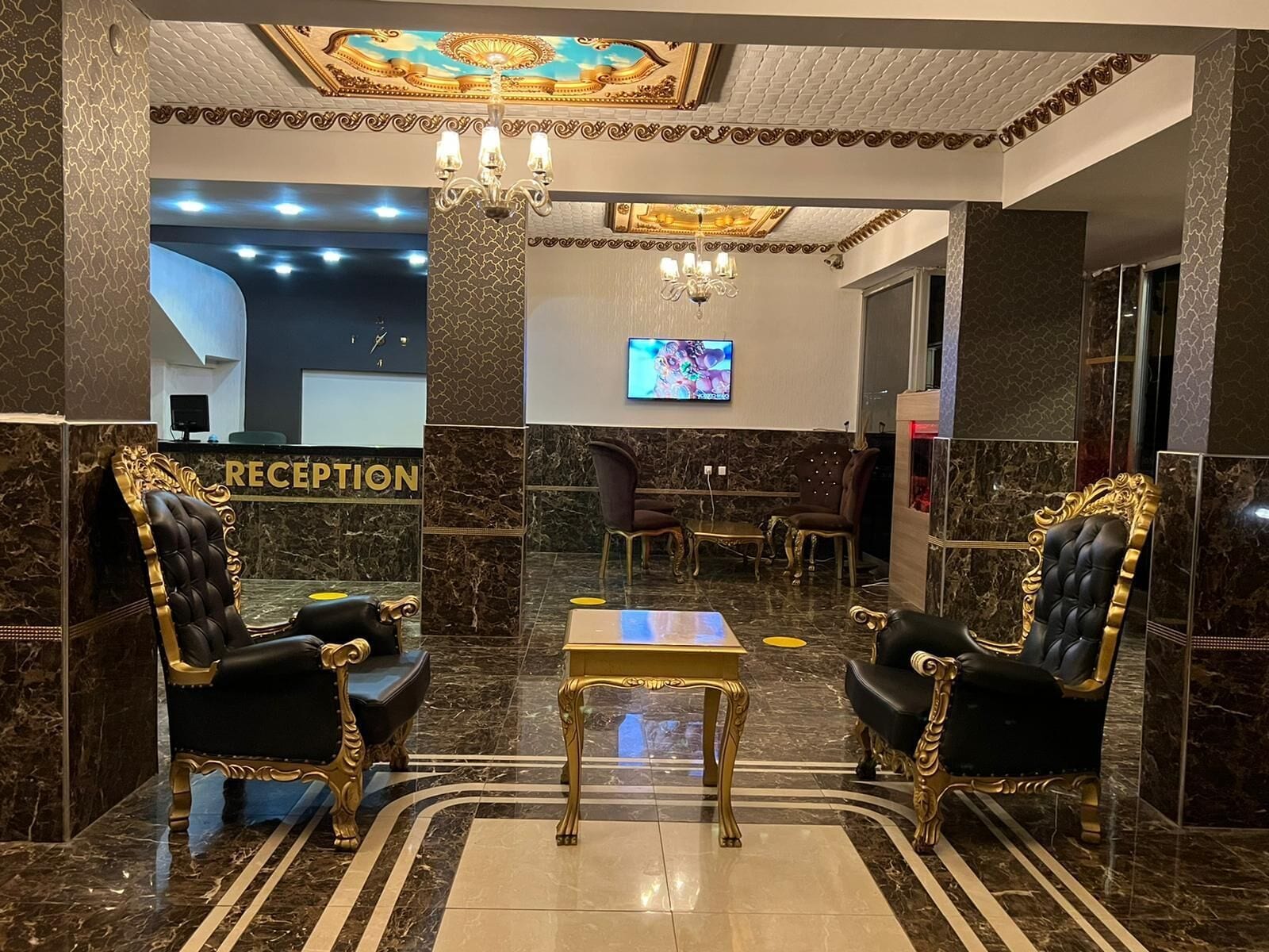 A reception area with a marble floor, two ornate black and gold chairs, a small table, and a television on the wall.