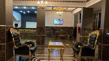 A reception area with a marble floor, two ornate black and gold chairs, a small table, and a television on the wall.
