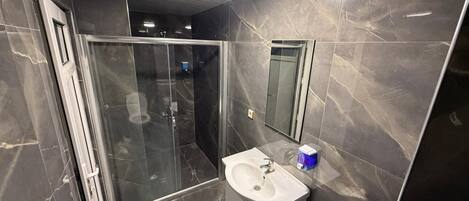 A modern bathroom with a glass shower enclosure, a white sink, and a mirror.