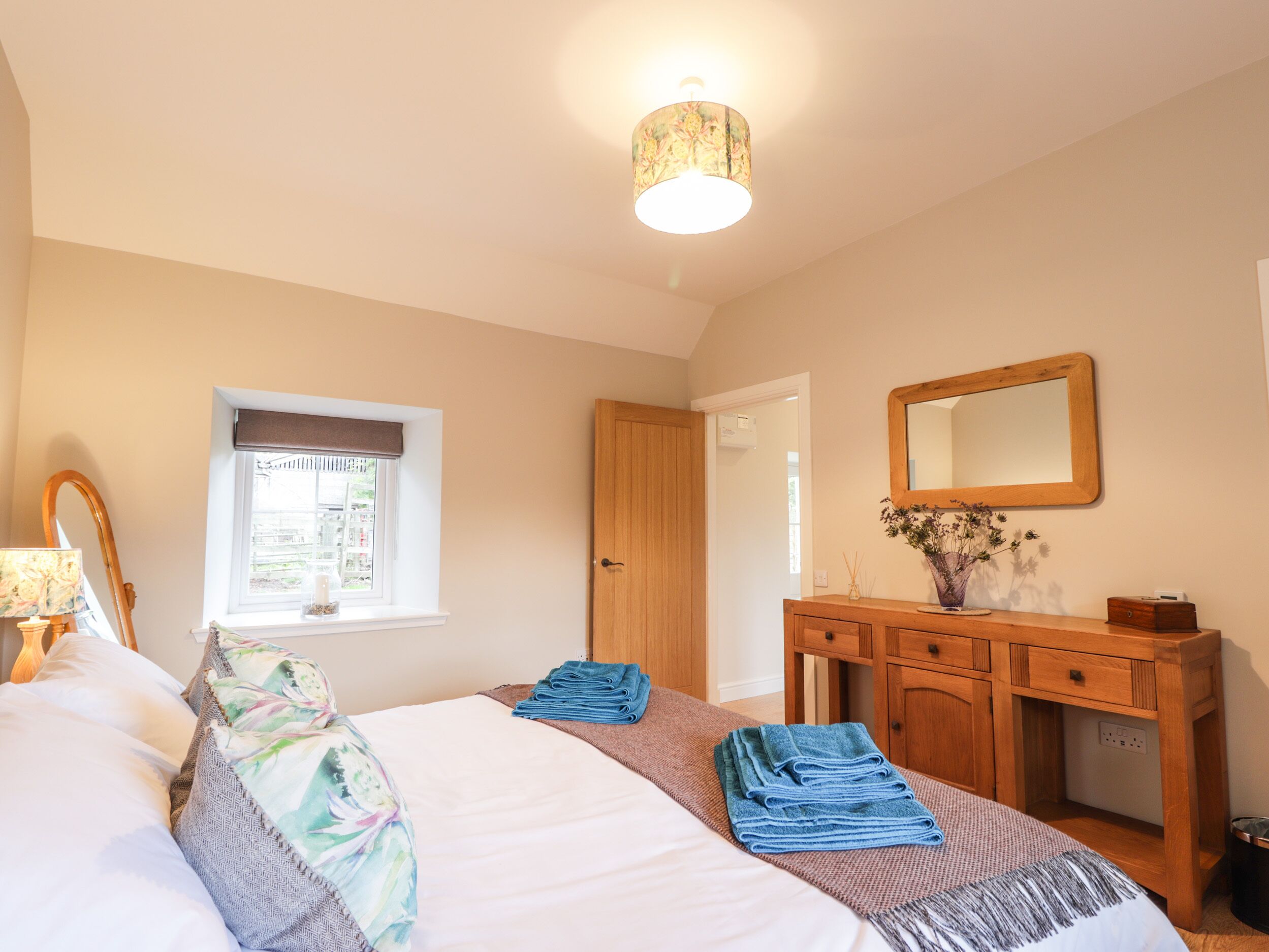 A bedroom with a bed, a bedside table, a dresser, a mirror, and a window.