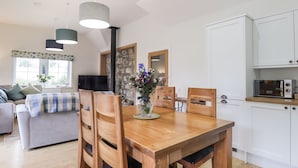 A modern kitchen with white cabinets, a wooden dining table, and a built-in microwave. - Bonnach (Muir of Ord)